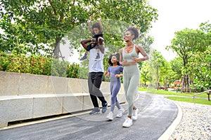 Happy African American family in sportswear running in public park. father carrying son with mother and daughter. Family