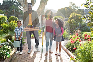 Happy african american family standing with garden tools and looking at camera