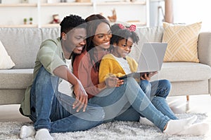 Happy african american family of three relaxing with laptop at home