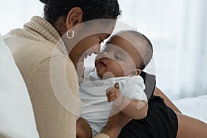 Happy African American family, young mother holding cute newborn baby girl in Arms with care smiling and sitting on bed at bedroom