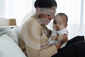 Happy African American family, young mother holding cute newborn baby girl in Arms with care smiling and sitting on bed at bedroom