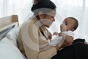 Happy African American family, young mother playing holding cute newborn baby girl in Arms smiling and sitting on bed at bedroom