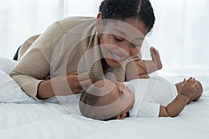 Happy African American family, young mother smiling holding her cute newborn baby girl hand and lying on bed together at bedroom