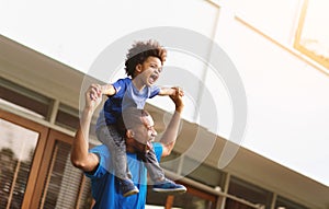 Happy African American Father carrying or piggyback his little son laughing playing outside