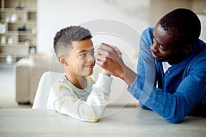 Happy african american father competing in arm-wrestling with his son, enjoying time together at home