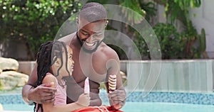 Happy african american father and daughter eating ice creams and embracing at swimming pool