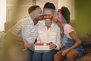 Happy African American father and daughter kissing mother on cheeks