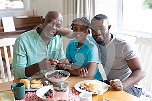 Happy african american father, grandfather and boy sitting at table and eating