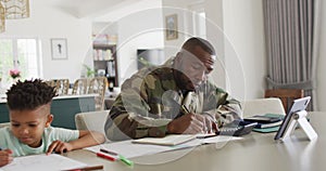Happy african american father and his son sitting at table, working and doing homework
