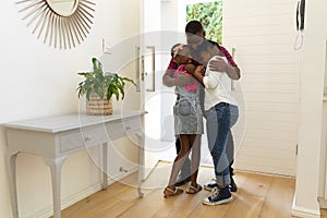 Happy african american father hugging son and daughter in hallway of home