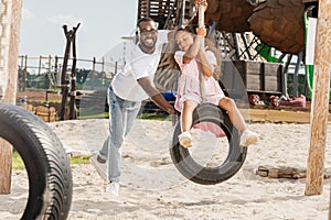 happy african american father pushing daughter on tire swing photo