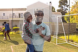 Happy african american father and son spending time together and playing football outside