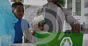 Happy african american father and son standing in kitchen sorting rubbish in recycling box