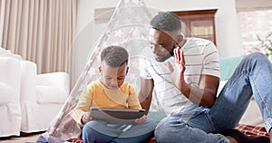 Happy african american father and son using tablet and doing high five at home, slow motion