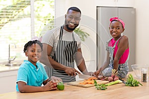 Happy african american father teaching daughter and son cooking in the kitchen
