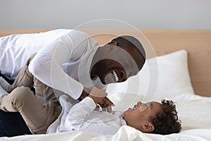 Happy African American father tickling laughing adorable son in bed