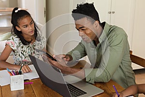 Happy african american father using tablet and daughter doing homework at home smiling