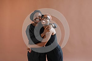 Happy african american friends or sisters hugging laughing looking at camera on brown background