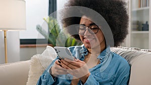 Happy African American girl holding cell mobile phone using smartphone device gadget at home smiling young woman using