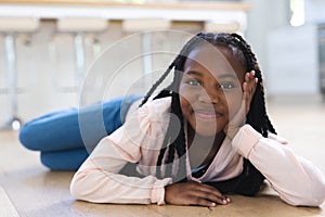Happy african american girl lying on floor with hand on face at home, copy space