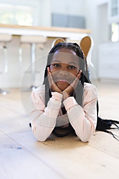 Happy african american girl lying on floor with hands on face at home, copy space