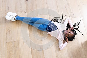 Happy african american girl lying on floor with hands on face at home, copy space