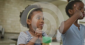 Happy african american girls eating and waving hands in kitchen