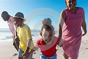 Happy african american grandchildren holding hands while pulling grandparents at beach