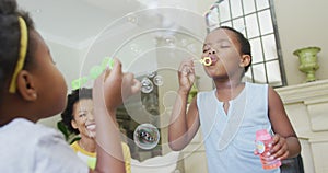 Happy african american grandmother with adult daughter and granddaughters blowing bubbles