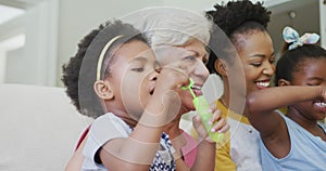 Happy african american grandmother with adult daughter and granddaughters blowing bubbles