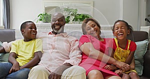Happy african american grandparents and grandchildren embracing on sofa