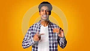 Happy african-american guy holding credit card and point on it