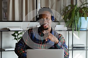 Happy African American hipster student guy in headphones watching webinar
