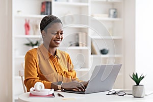 Happy african american lady freelancer using laptop at home