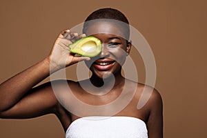 Happy african american lady holding half of avocado in front of eye