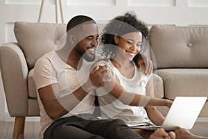 Happy african american loving family couple holding computer, watching photos.