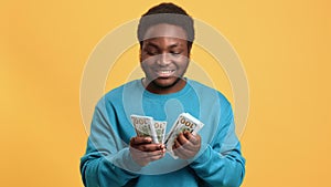 Happy African American man counting dollars and smiling, look at camera, medium portrait in studio