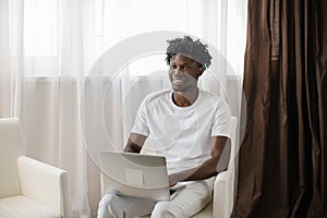 Happy african american man with dreadlocks, enjoying watching educational webinar on laptop. Smiling young mixed race