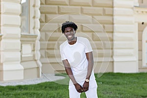 Happy African American man with dreadlocks stands on the street and laughs. Against the backdrop of greenery and