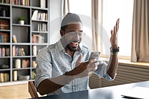 Happy African American man excited by good news, using phone photo