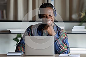 Happy African American man in headphones looking at laptop screen