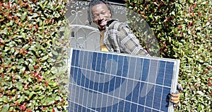 Happy african american man holding photovoltaic panel entering property, slow motion