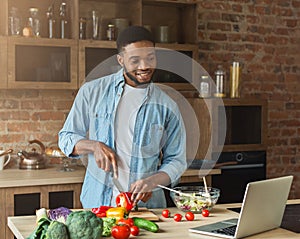 Happy african-american man preparing salad in kitchen