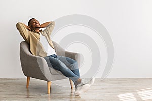 Happy African American Man Relaxing Sitting In Chair, Gray Background