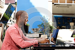 Happy african american man sitting at cafe with laptop computer