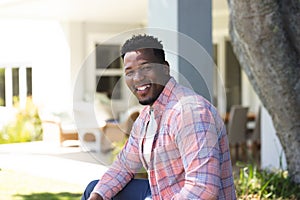 Happy african american man sitting with hands on leg in sunny garden, copy space