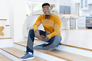 Happy african american man sitting on stairs at home, copy space