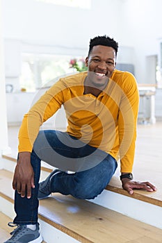 Happy african american man sitting on stairs at home, copy space