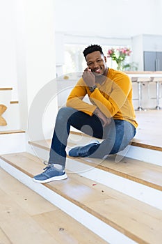 Happy african american man sitting on stairs and scratching face at home, copy space