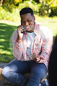 Happy african american man sitting on stairs and talking on smartphone in sunny garden, copy space